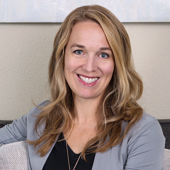 photo of a woman with long blonde hair sitting with her arm around her seat top smiling at the camera